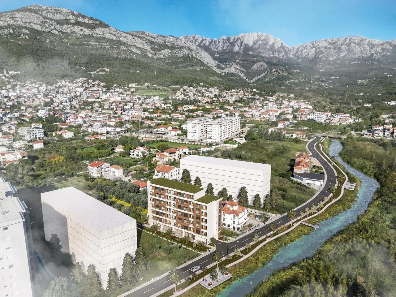 Aerial view of residential buildings near a river and mountains, showing the town layout.