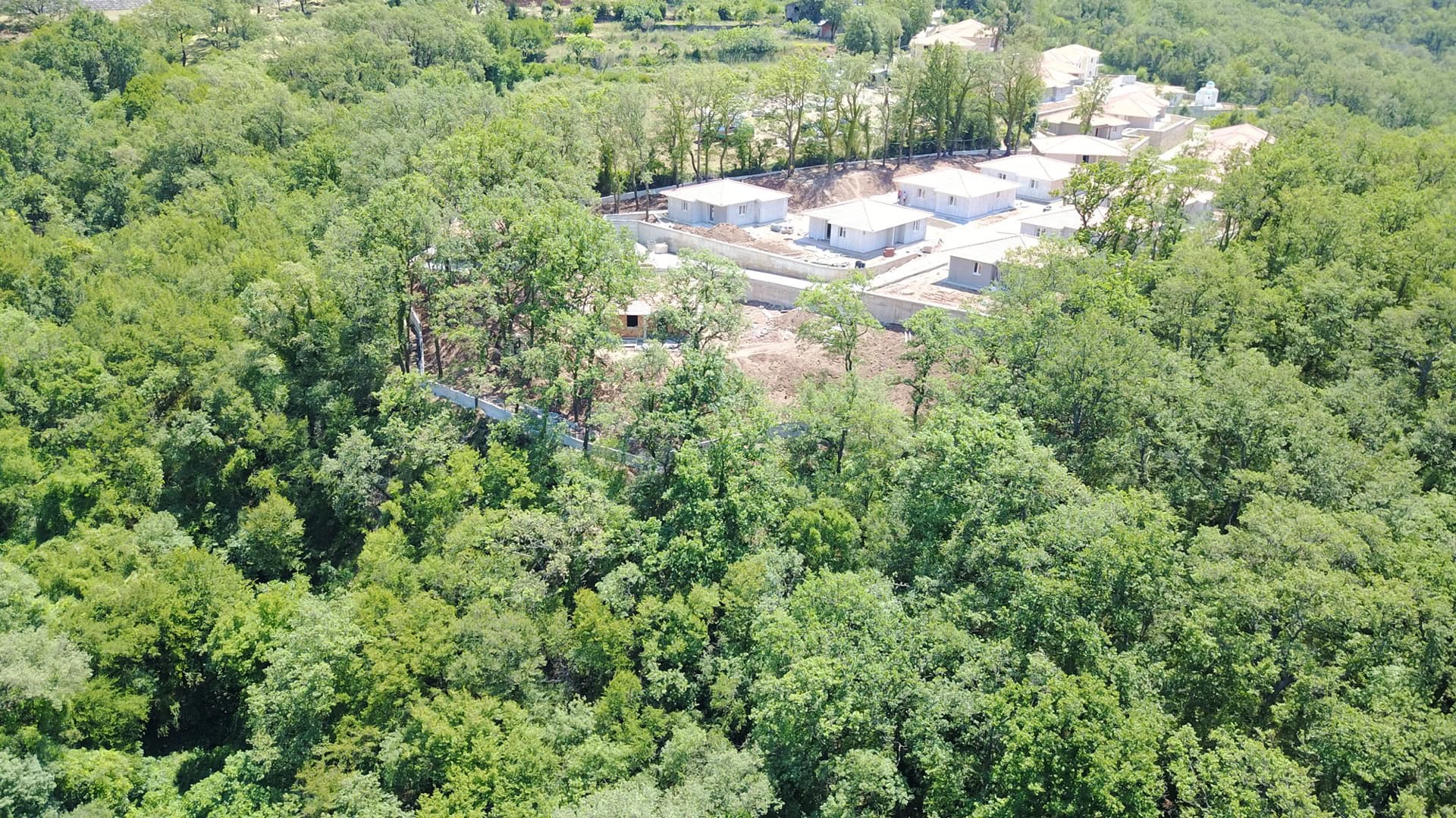 Villas under construction surrounded by forest on a plot of land in Bar, Montenegro, aerial view.