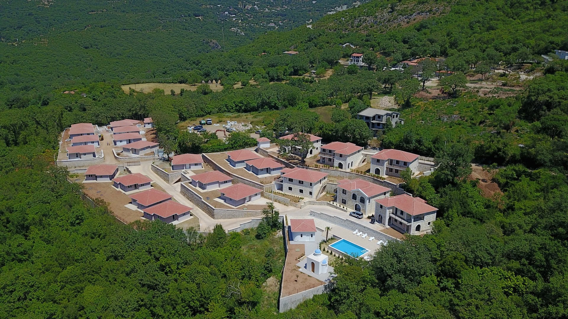 Aerial view of a residential complex with villas, a swimming pool, and stone finishes, surrounded by mountains and forests, Bar, Montenegro