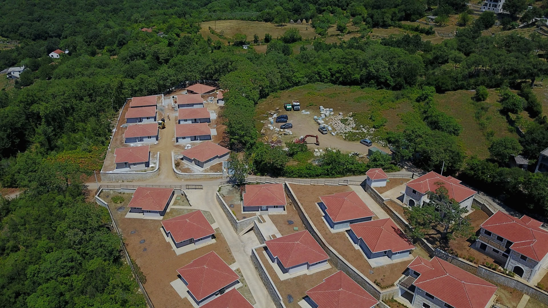 Aerial view of a cottage community under construction with red roofs surrounded by forest, Bar, Montenegro.