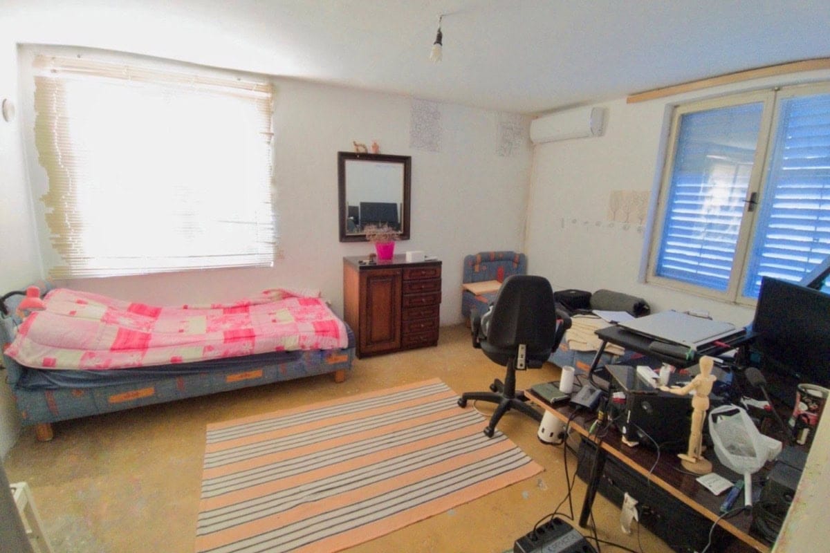 Bedroom in a house in Dobri Vody, Montenegro: bed, workspace with an office chair, and a mirror on the wall.