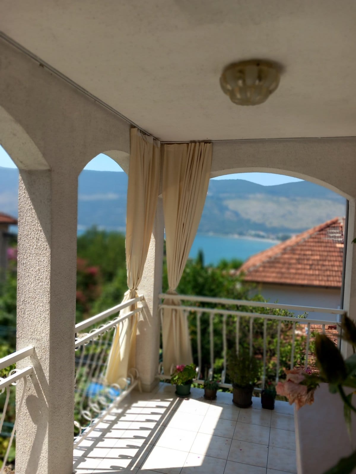 Balcony with panoramic sea and mountain views in a building, Igalo, Montenegro: a bright terrace with arches and live flowers.