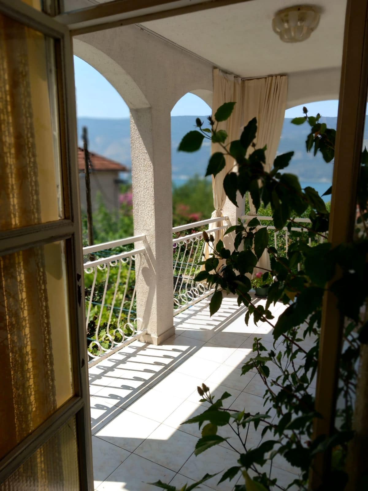 View from the balcony of a house in Igalo, Montenegro: an arched terrace with wrought-iron railing and panoramic views of the sea and mountains.