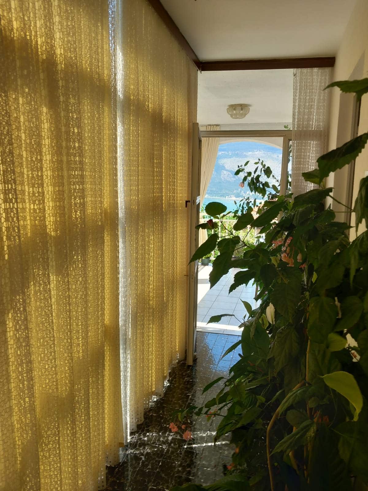 View from the living room of a house in Igalo, Montenegro: a terrace with panoramic sea views, houseplants, and light curtains.