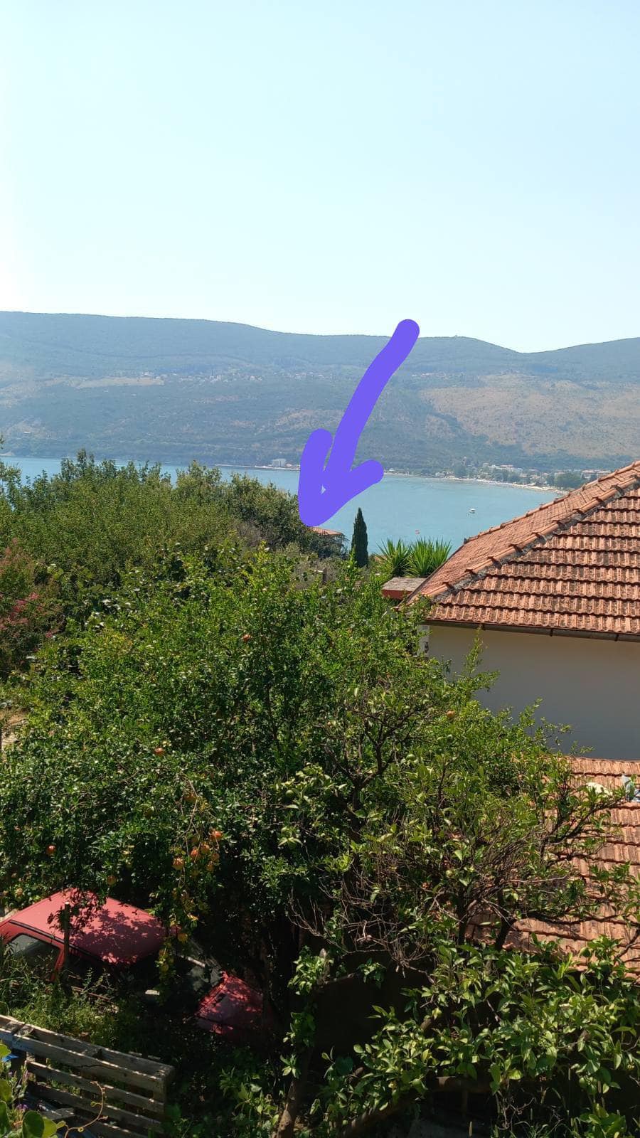 Panoramic view of the sea and mountains from a house in Igalo, Montenegro, with a garden and tiled roof in the foreground.