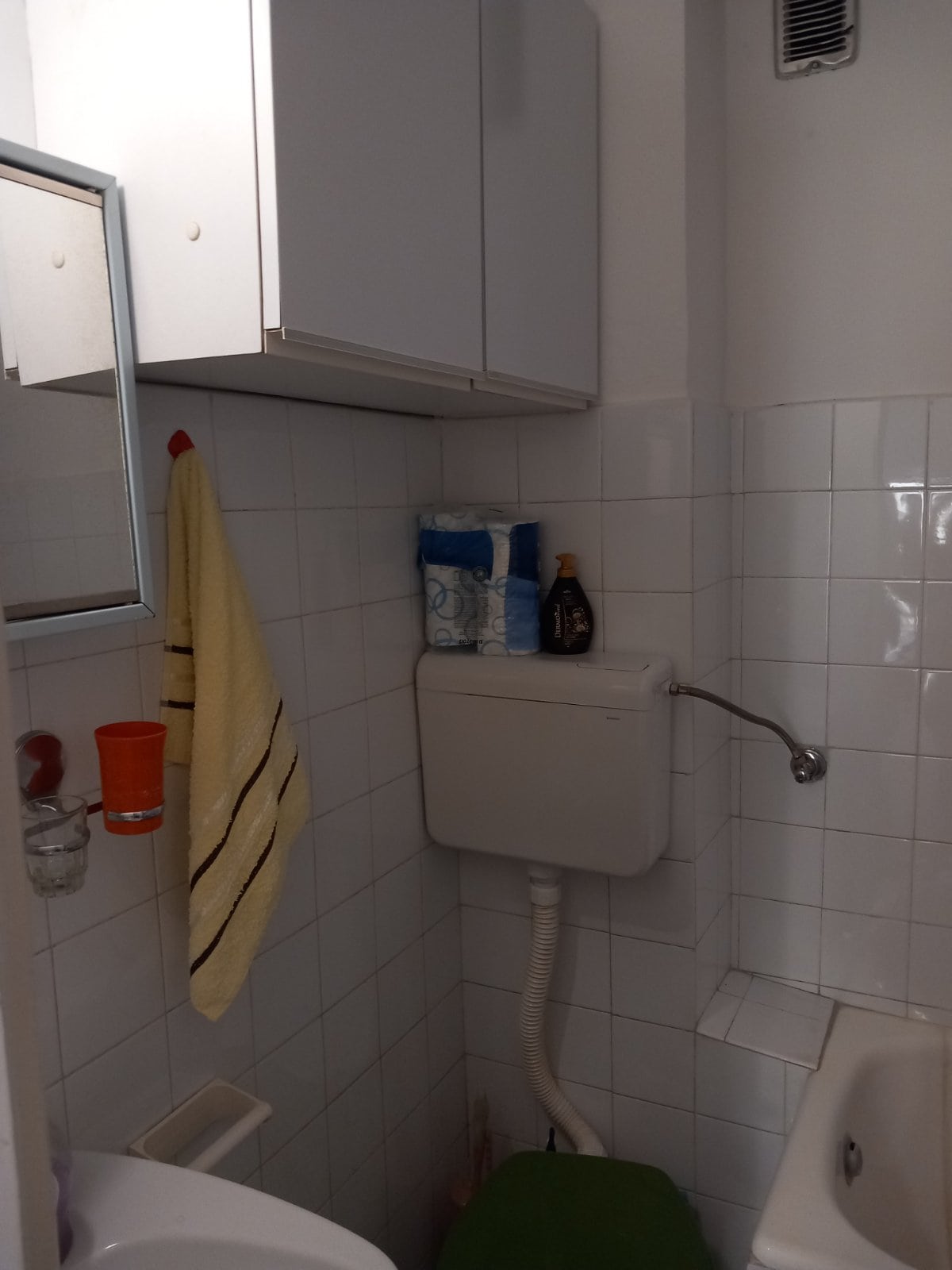 Bathroom in a house in Igalo, Montenegro: white tiles, wall cabinet, plumbing fixtures, and a mirror in the interior.