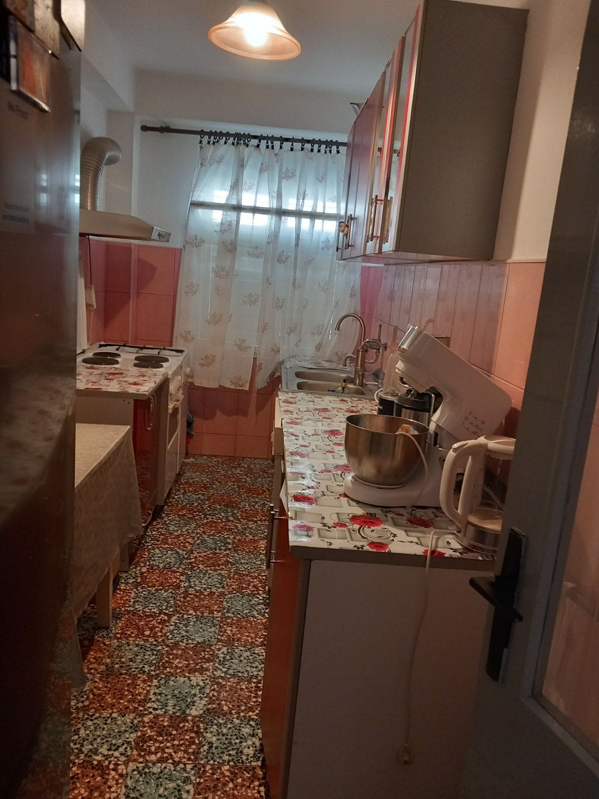 Cozy kitchen in a house in Igalo, Montenegro: kitchen cabinets, appliances, patterned tiles, and a window with curtains.