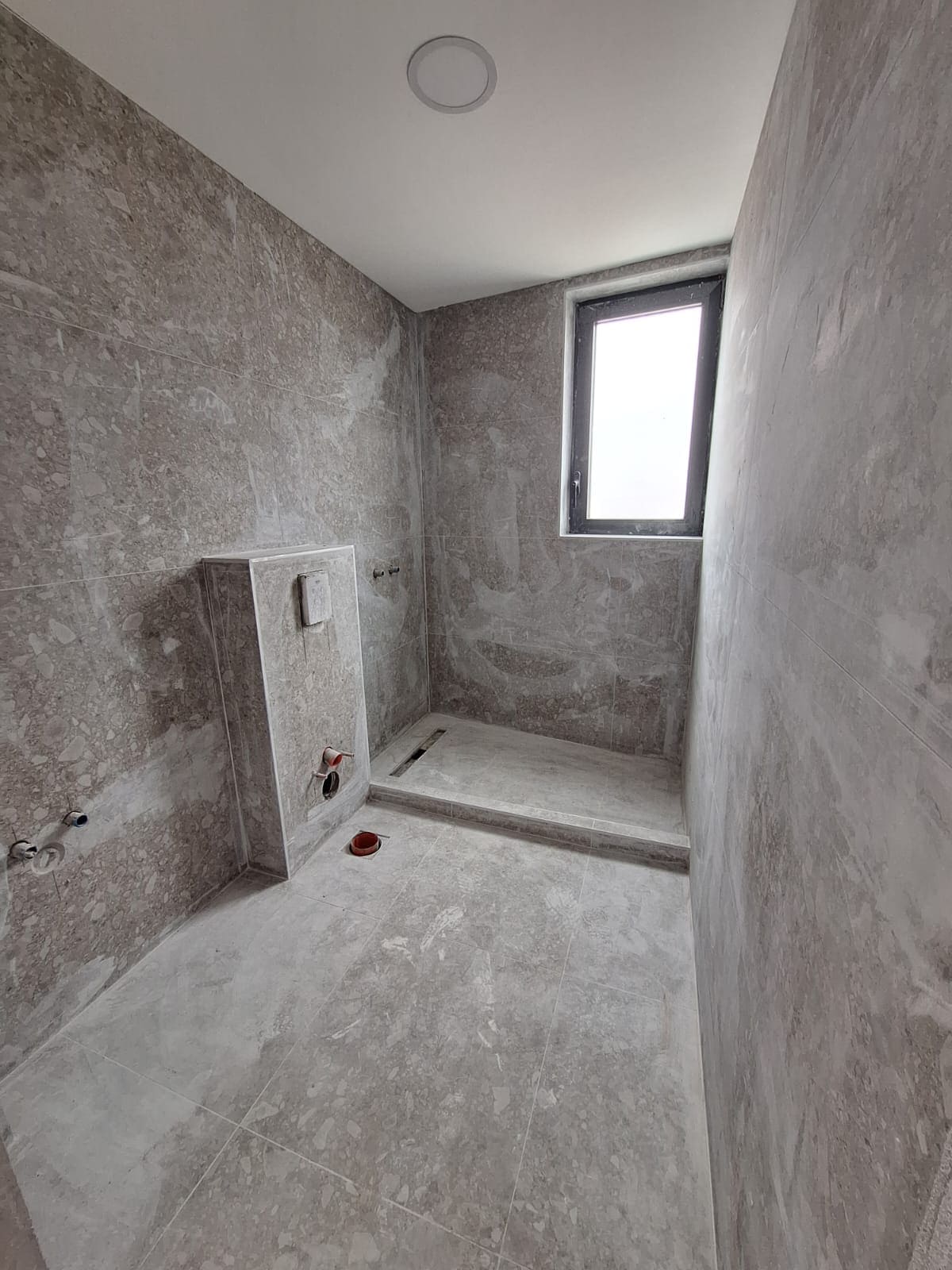 Bathroom under renovation in an apartment, Bar, Montenegro: gray tiles, shower area, and concealed toilet installation.