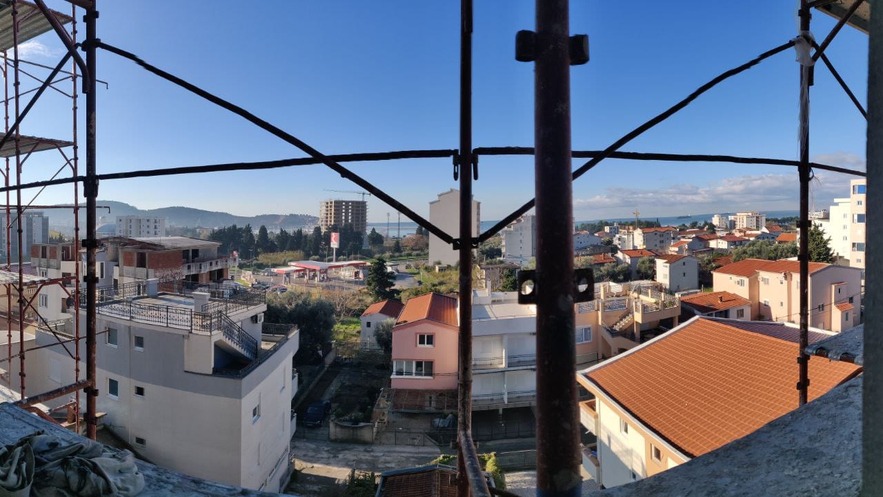 View from the balcony of a house under construction in Bar, Montenegro: a city panorama, tiled roofs, and mountains on the horizon.