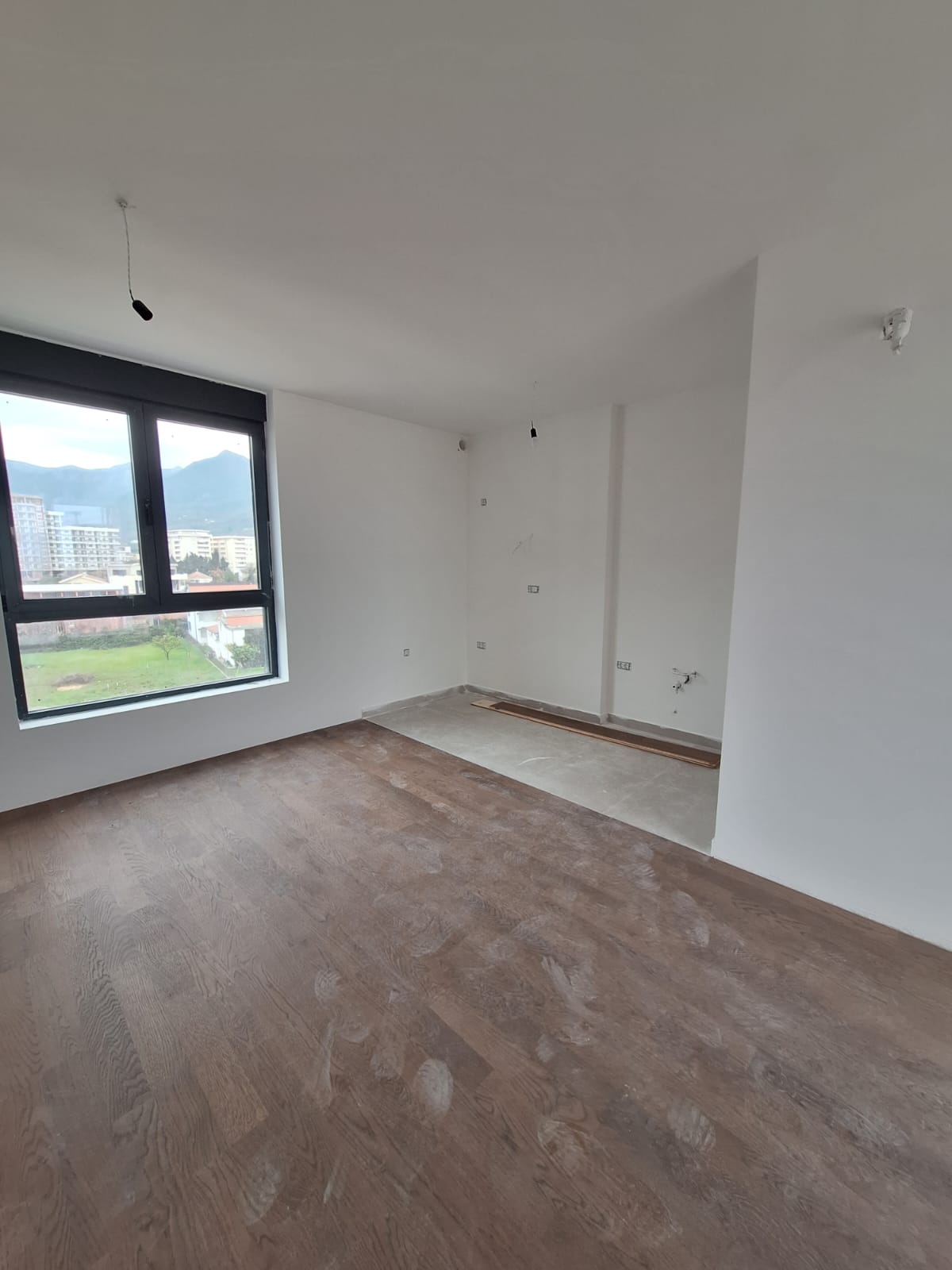 Bright living room with parquet flooring and a panoramic window in a new apartment in Bar, Montenegro, mountain view.