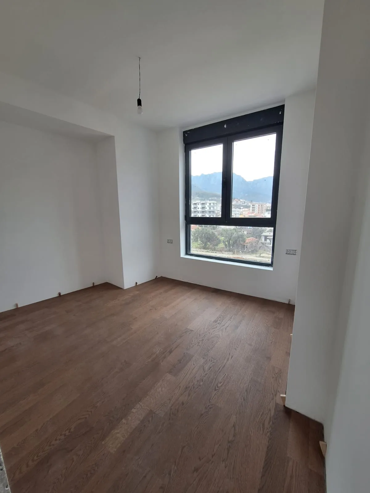 Empty room with wood flooring and a window overlooking mountains. No furniture or specific features of a bedroom or living room visible.