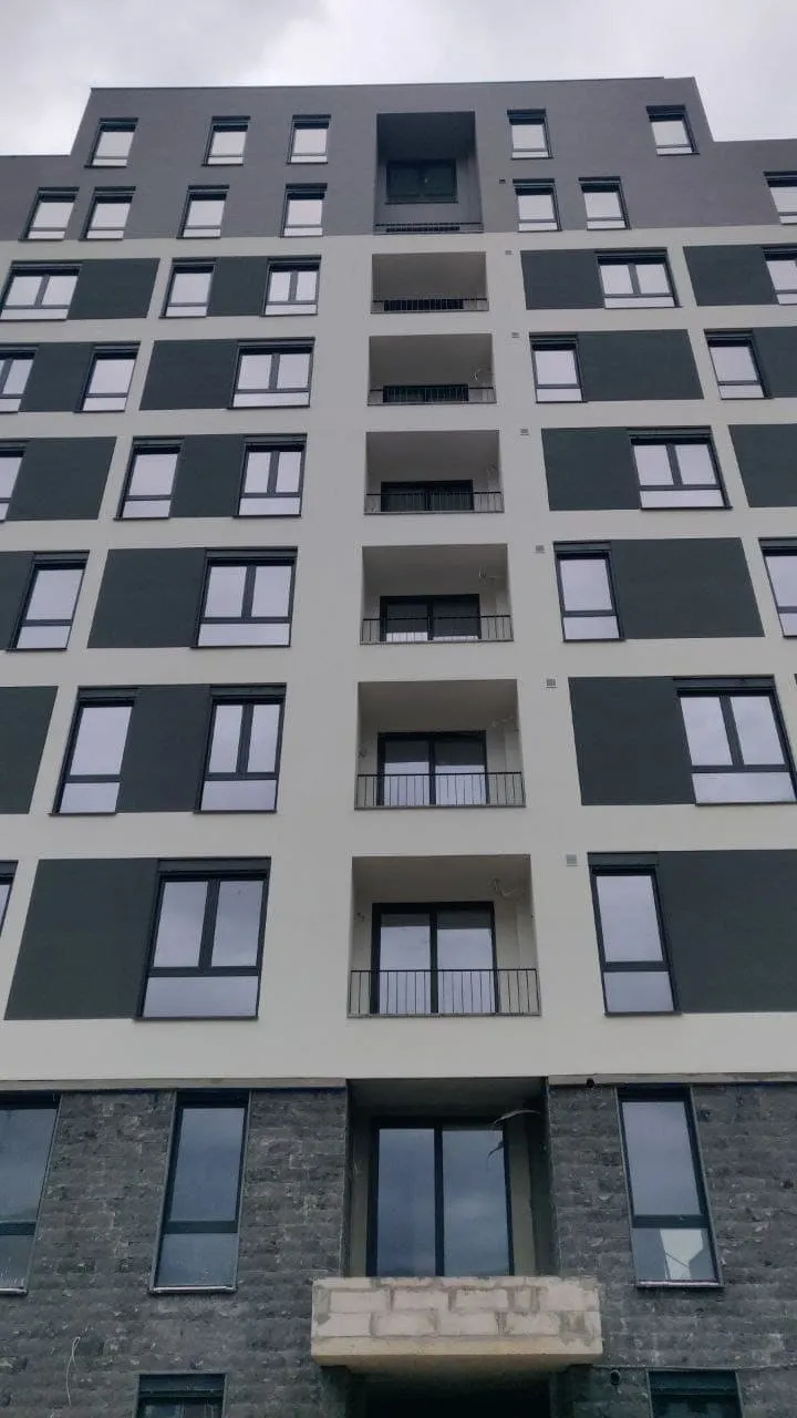 Exterior view of a multi-story residential building featuring balconies and windows against a cloudy sky.