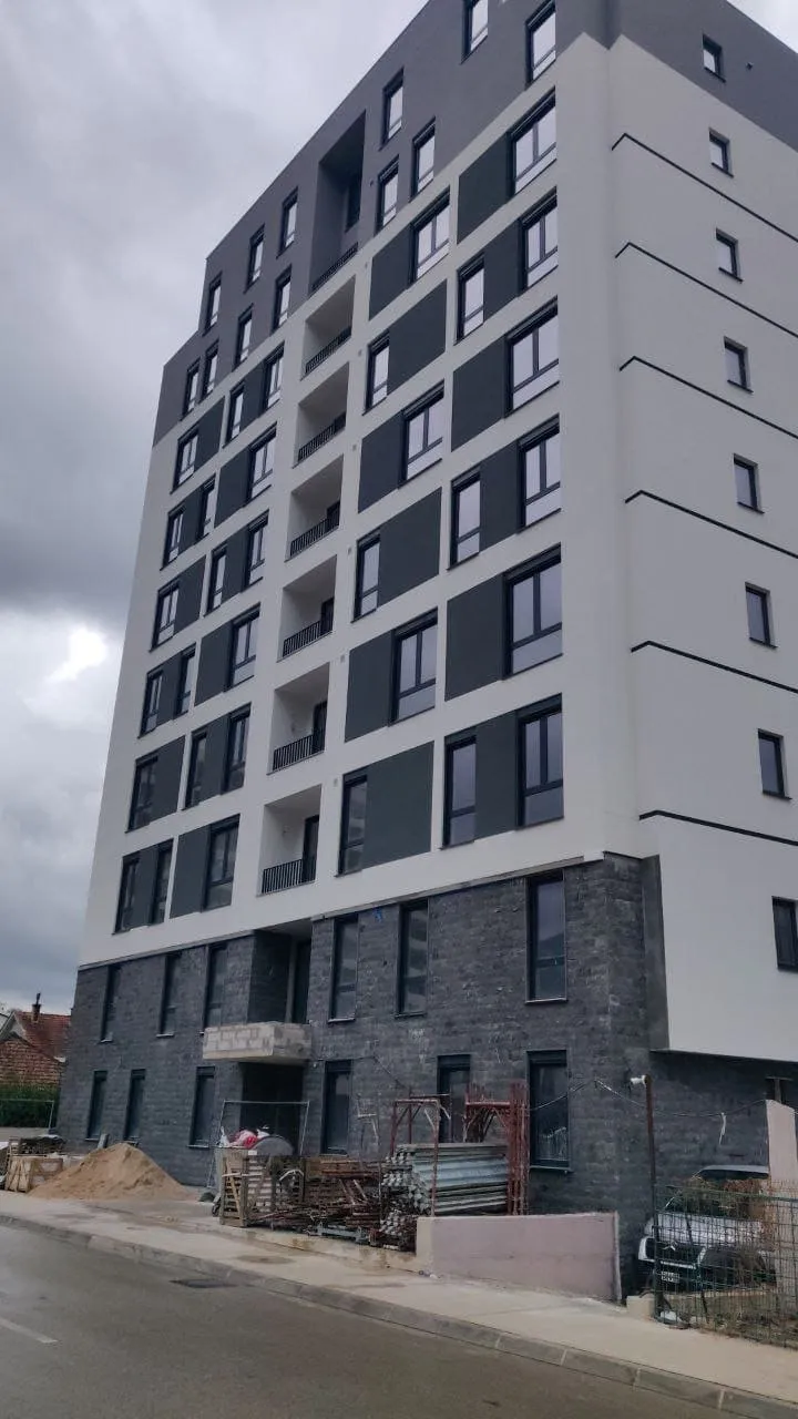 Exterior view of a multi-story residential building with balconies and construction materials at the base.