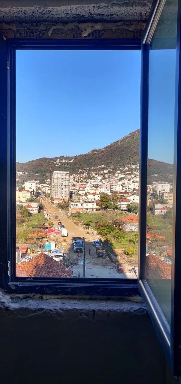 View through a blue window frame onto a street with vehicles and a mountain in the background. Rough sill visible.