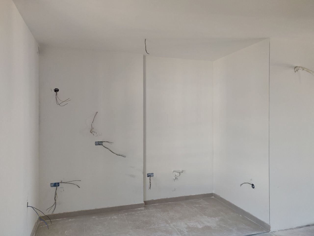 Living room in a new building in Bar, Montenegro: pre-finished condition, white walls, and electrical outlets prepared for renovation.