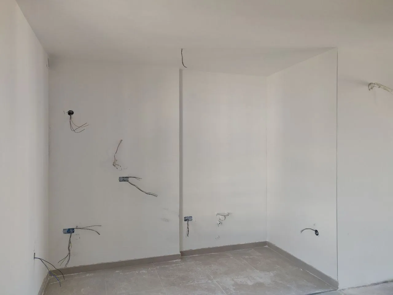 Empty room under renovation with white walls, exposed electrical wires, and tiled flooring.