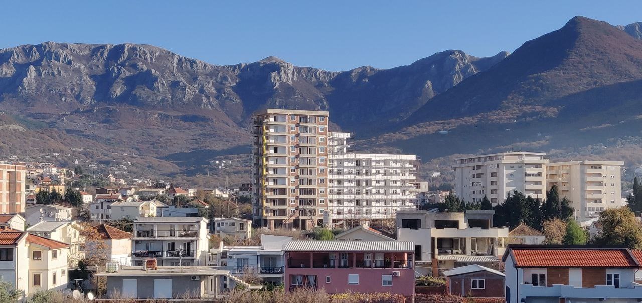 An under-construction multi-story residential complex in Bar, Montenegro, against a backdrop of picturesque mountain scenery.