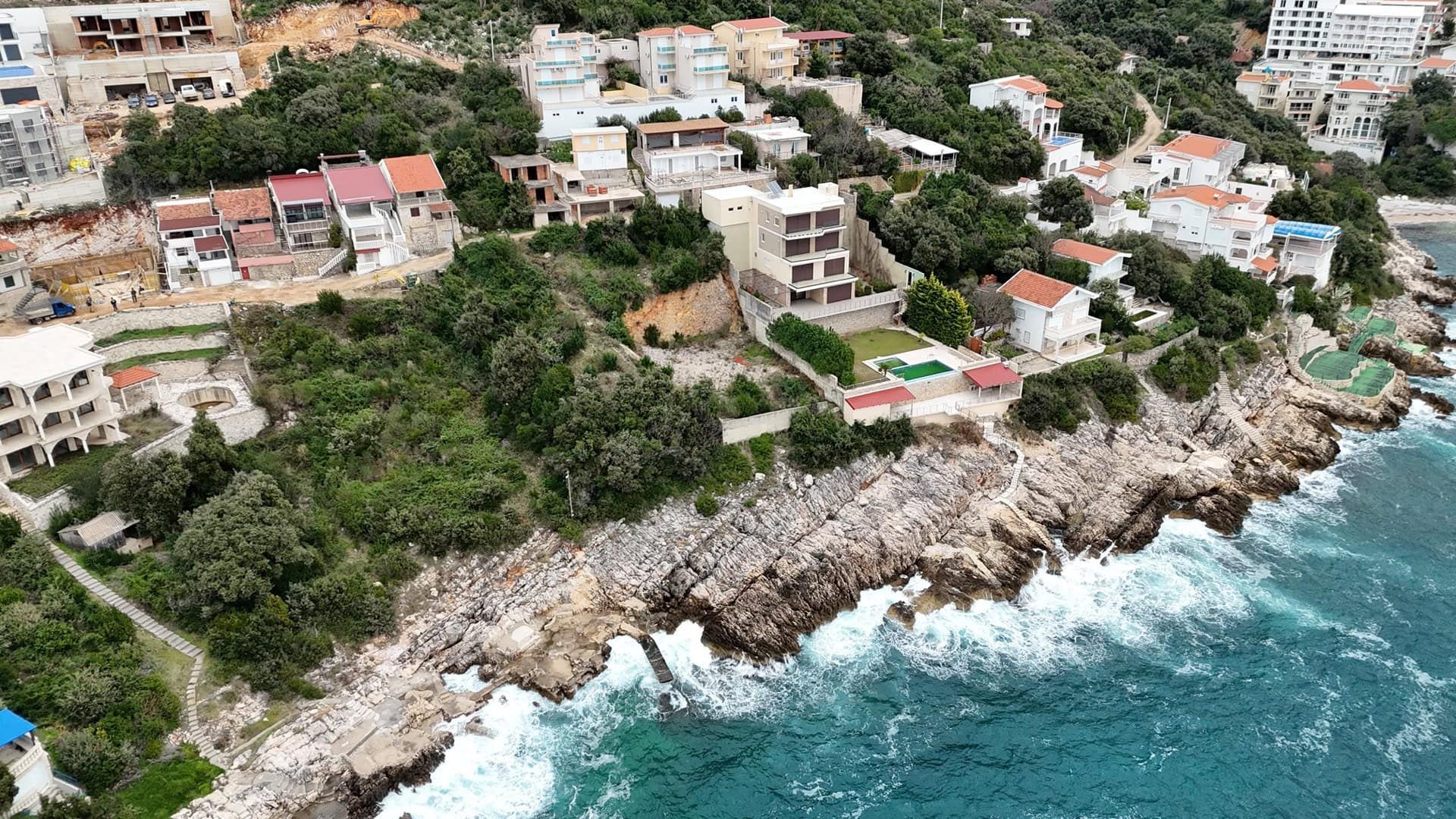 Aerial view of plot No. 2395 in Utjeha, Montenegro: a coastal property with a house and a pool by the sea.