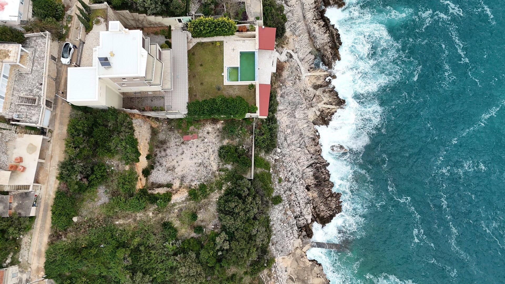 Plot No. 2395 in Utjeha, Montenegro: aerial view of a villa with a pool right by the sea and rocky shore.