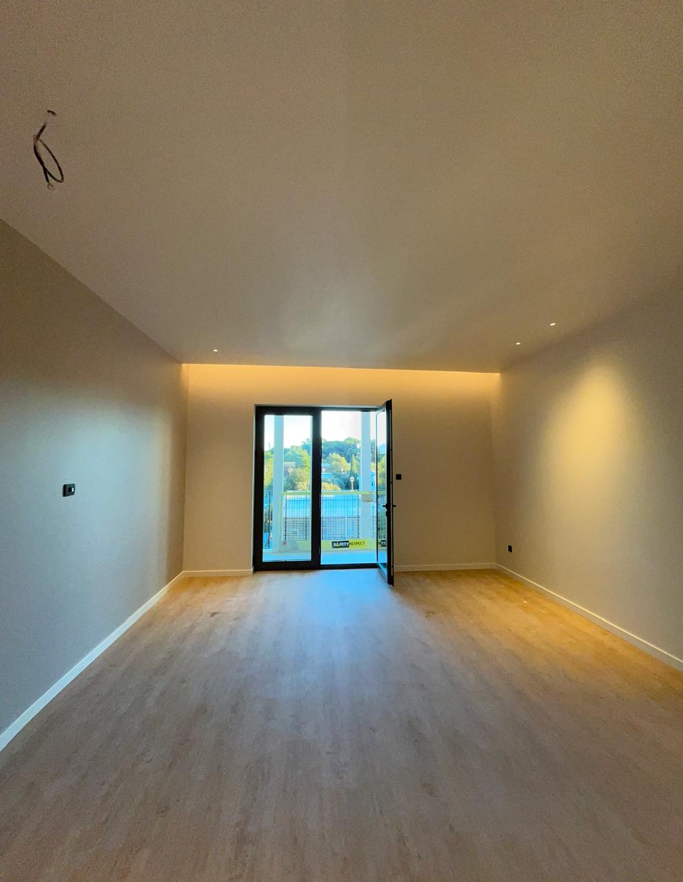 Modern living room in a new building in Tivat, Montenegro: bright interior, parquet flooring, and access to the balcony.