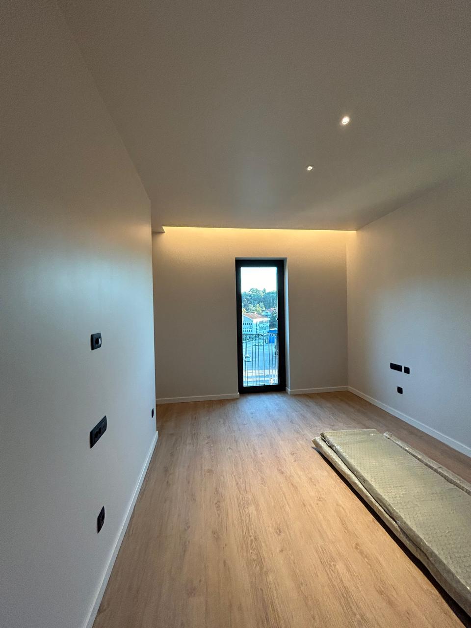 Modern bedroom in an apartment in Tivat, Montenegro: light finishes, laminate flooring, hidden lighting, and a view from the window.