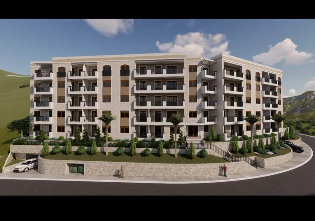 Exterior view of a multi-story residential building with balconies, landscaping, and cars on the road.