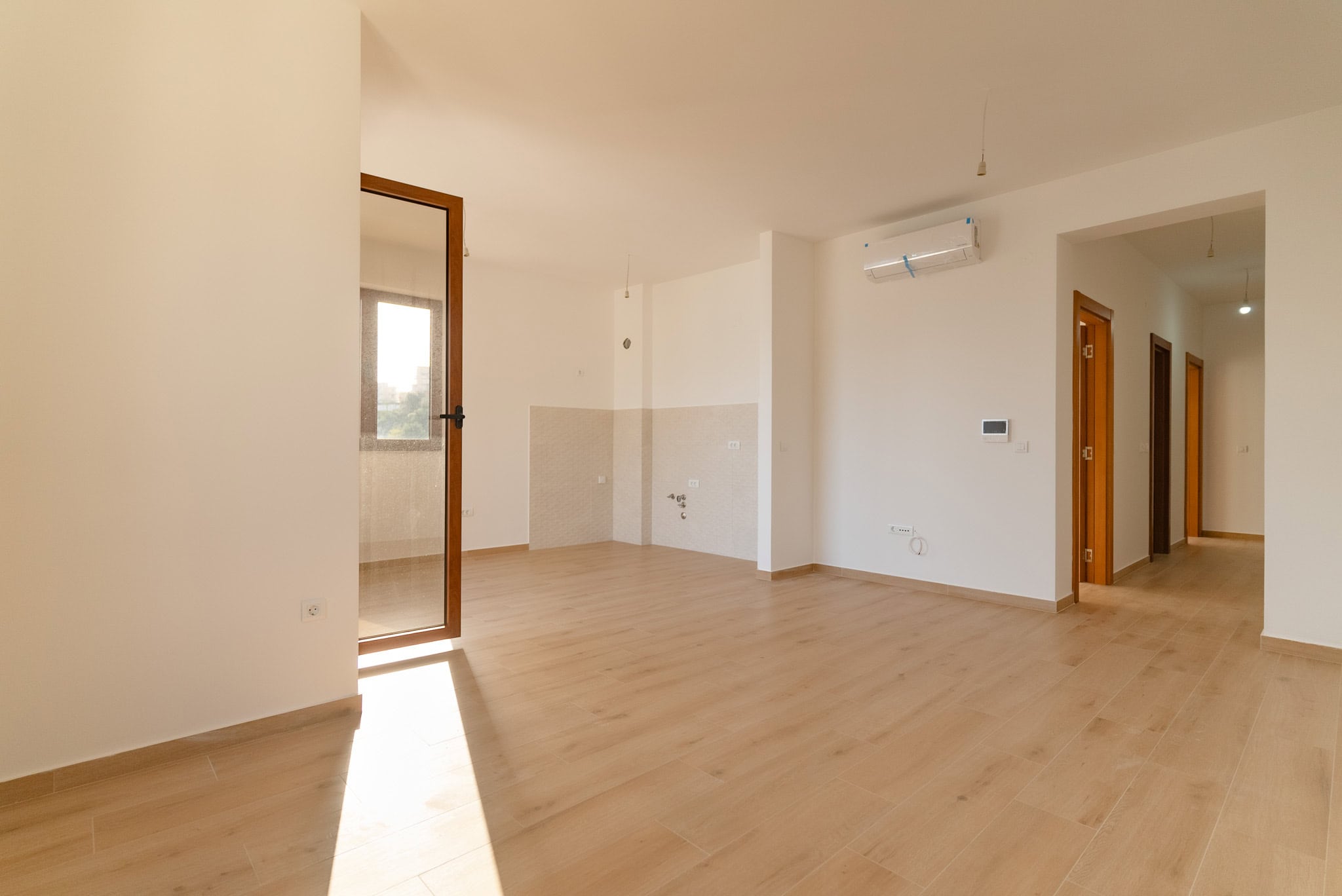 Bright living room in a new apartment in Budva, Montenegro: laminate flooring, white walls, air conditioning, and access to the balcony.