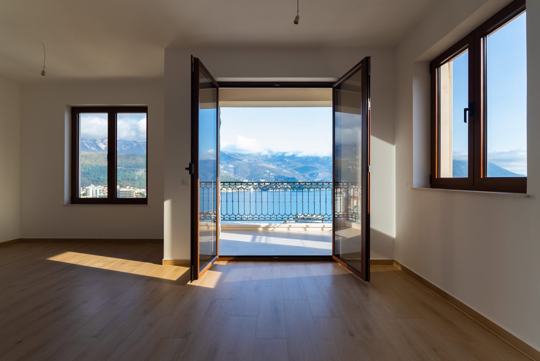 Bright living room with parquet flooring and access to a balcony with panoramic sea and mountain views in Budva, Montenegro.