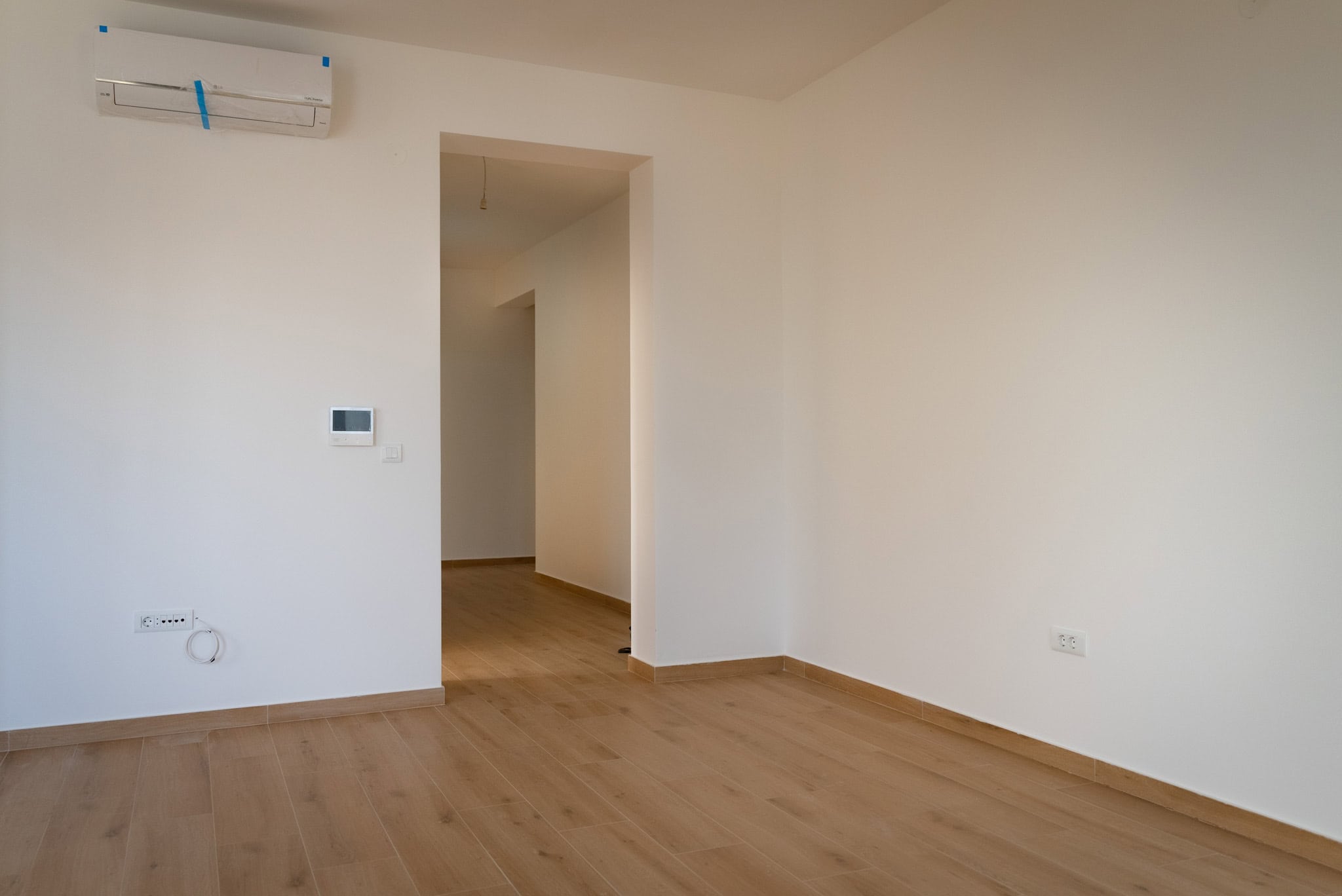 Bright living room in a new apartment in Budva, Montenegro: white walls, wood-look laminate flooring, and installed air conditioning.