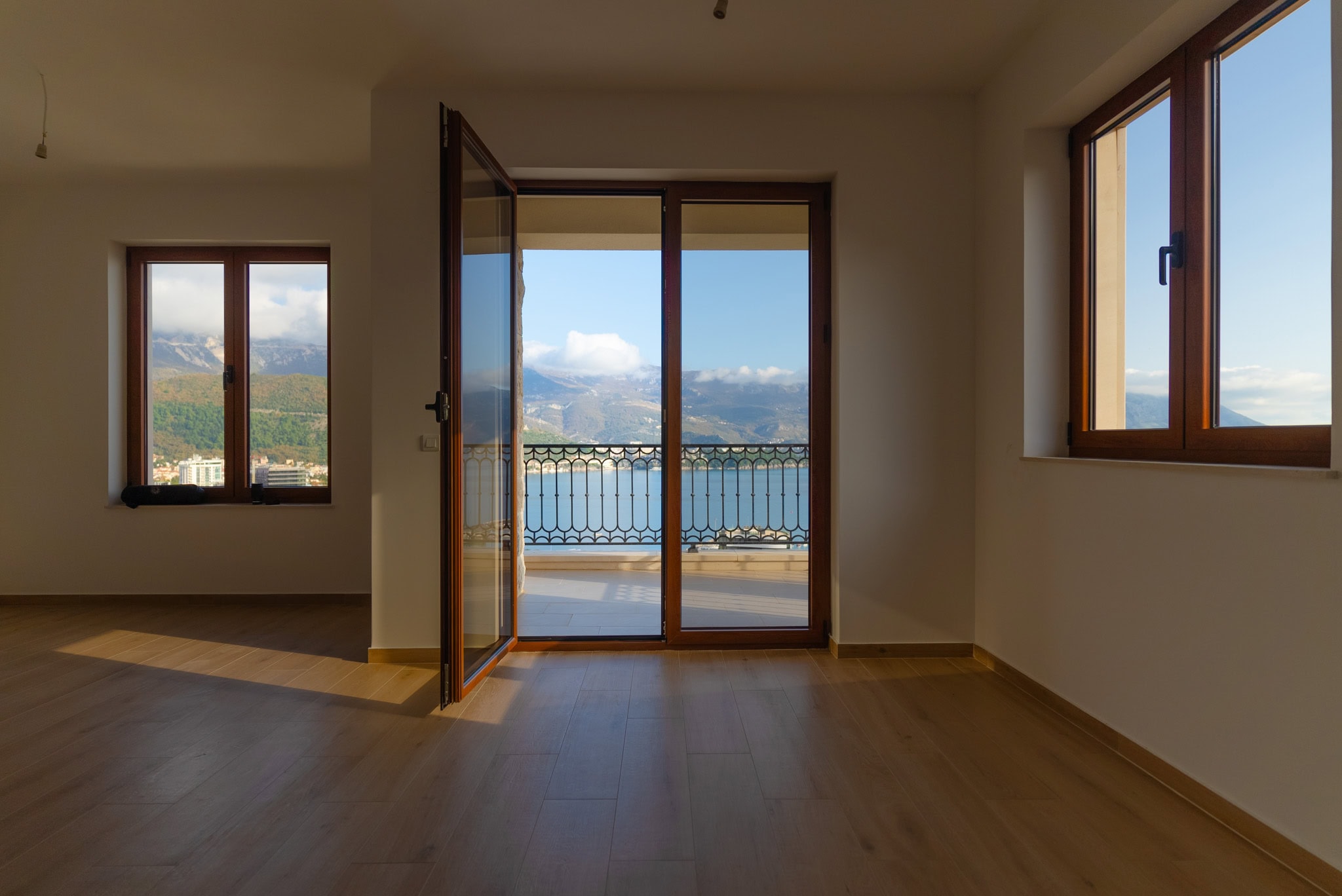 Bright living room in Budva, Montenegro, with access to the balcony, panoramic sea and mountain views, wooden floor.