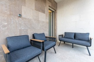 Cozy villa terrace in Becici, Montenegro: modern patio furniture with grey cushions and natural stone wall cladding.