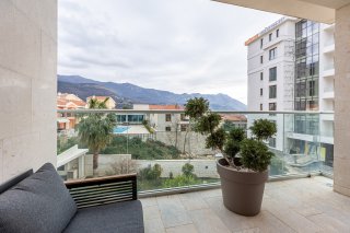 Villa balcony in Bečići, Montenegro: mountain view, modern furniture, glass railing, and decorative plant.