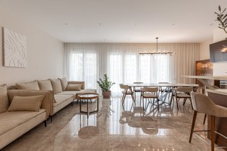 Modern living room with a beige sofa and dining area in a villa in Bečići, Montenegro, marble flooring and panoramic windows.