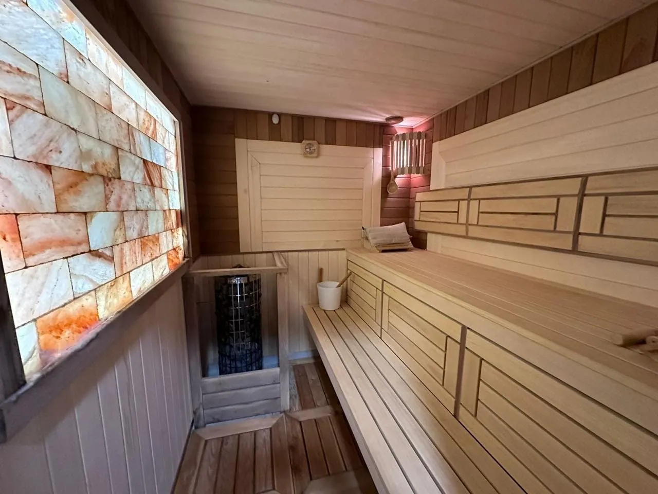 Wooden sauna with salt brick wall lighting, tiered benches, and a wood-fired heater.