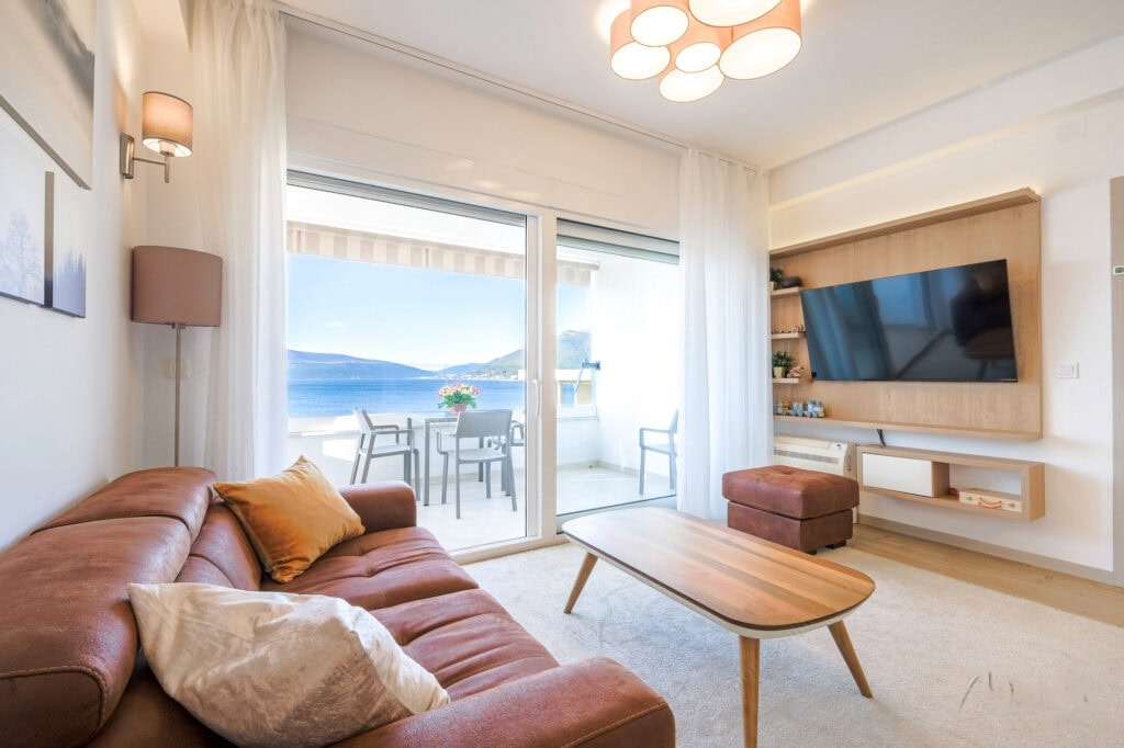Living room with a leather sofa and sea view in an apartment in Tivat, Montenegro, with access to a furnished terrace.
