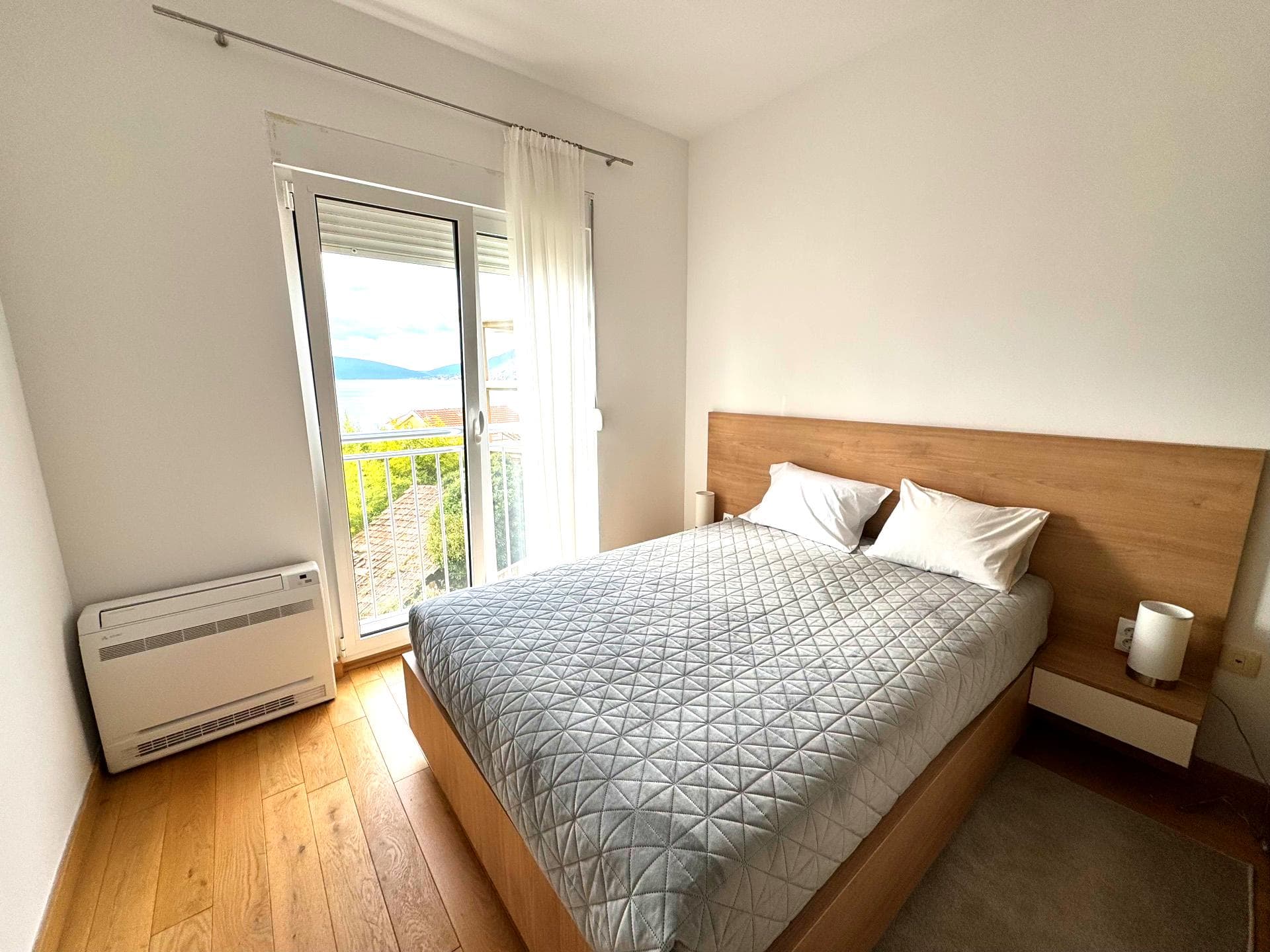 Bedroom with a double bed and sea view in an apartment in Tivat, Montenegro: bright interior, parquet flooring, balcony.