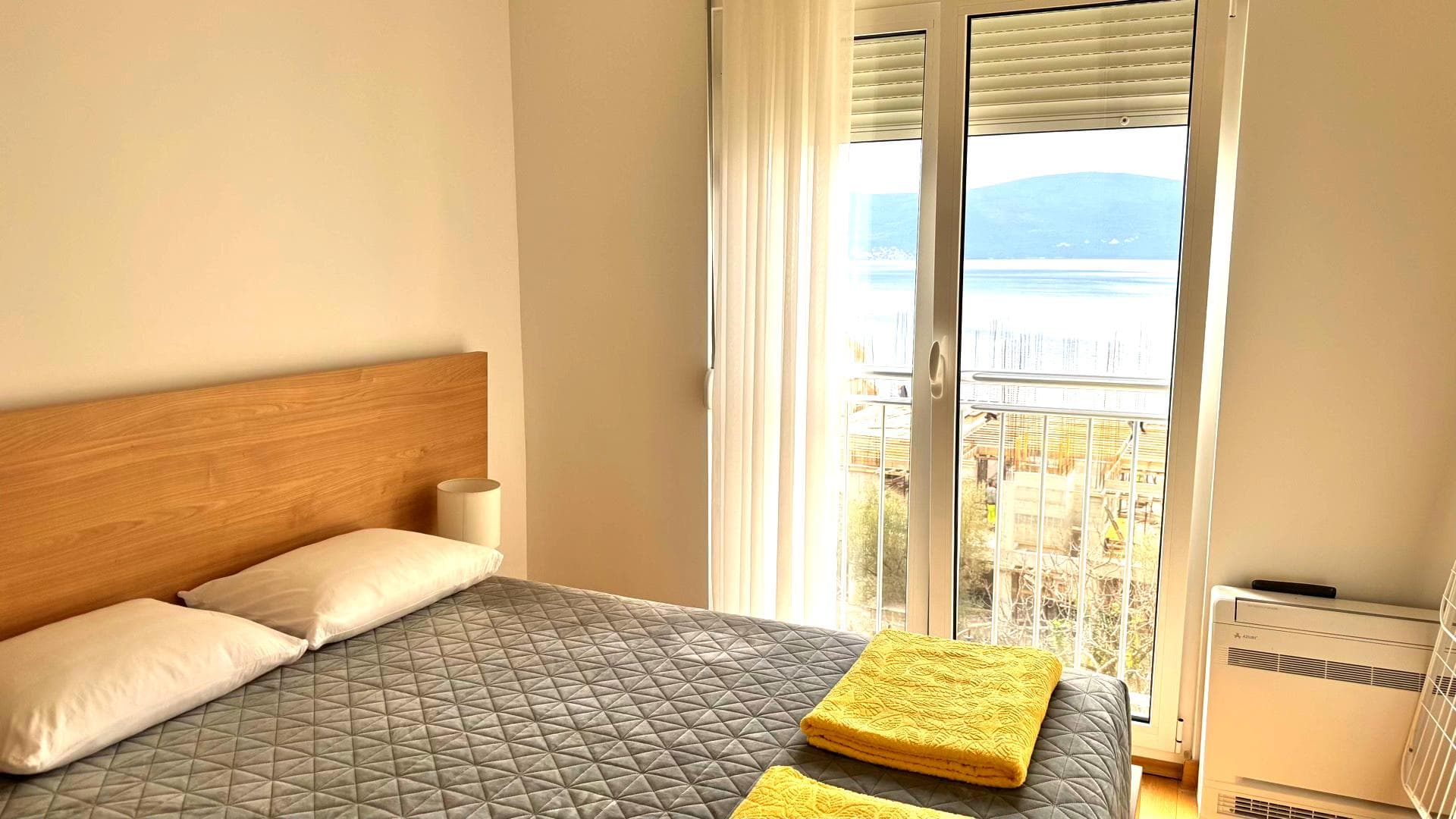 Bedroom in an apartment in Tivat, Montenegro: a double bed, light finishes, and a balcony with panoramic sea views.