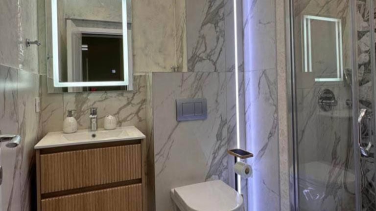 Modern bathroom in an apartment in Tivat, Montenegro: marble-effect finish, shower cabin, and backlit mirror.