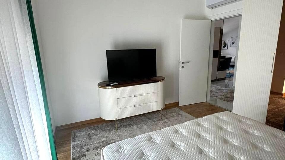 Modern bedroom with a white dresser and TV in an apartment in Tivat, Montenegro: stylish interior with parquet flooring.