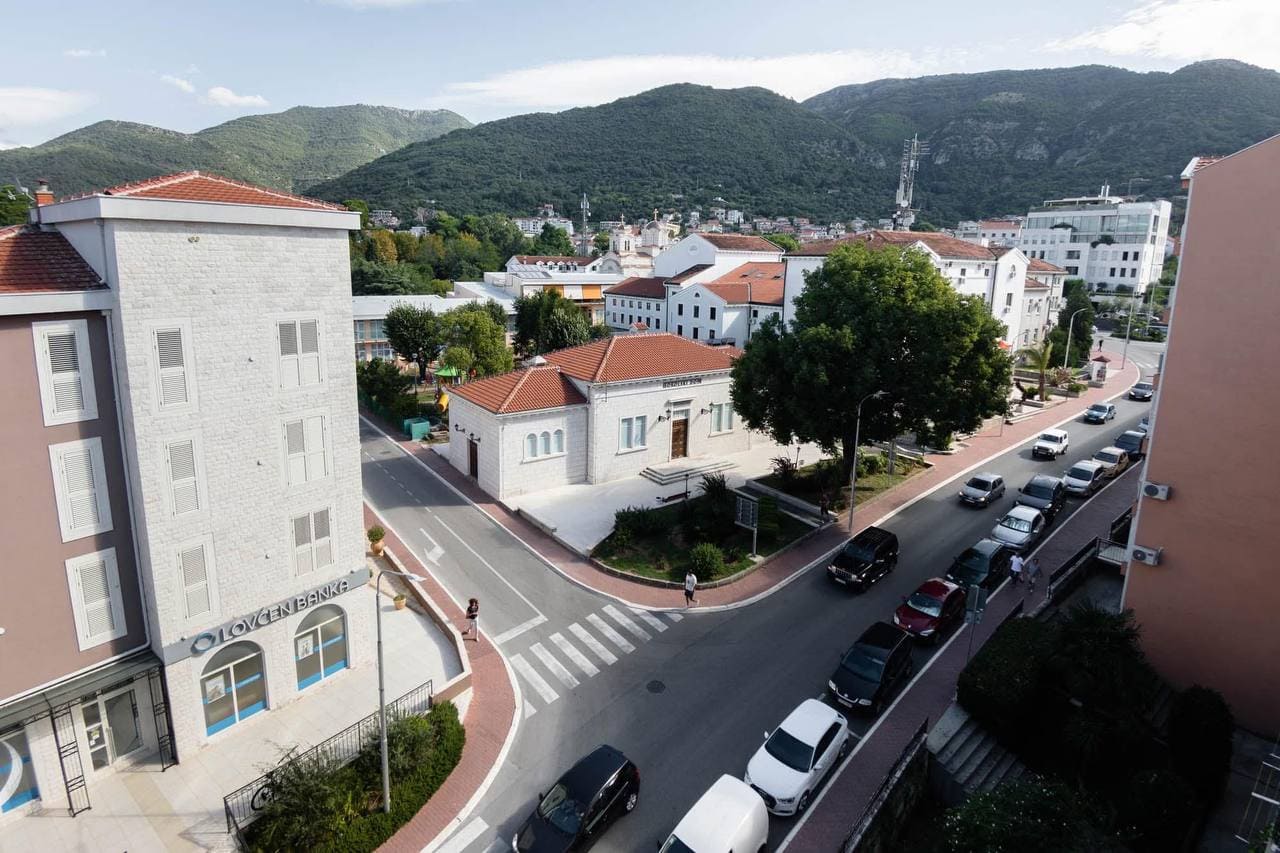 View from the window of a city street, the Lovćen Banka building, and mountains in Tivat, Montenegro.