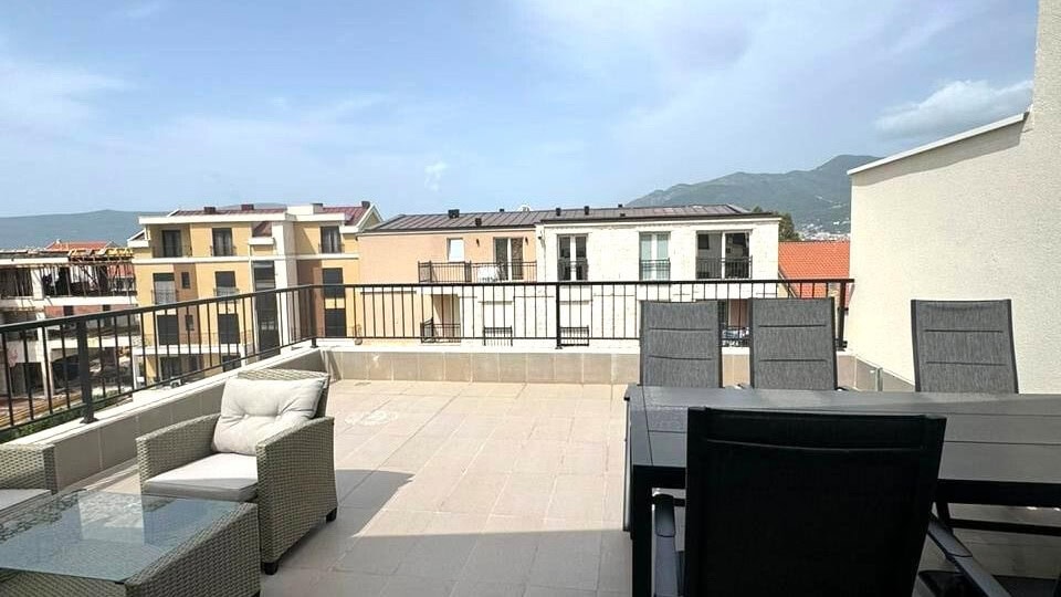 Spacious terrace with garden furniture in an apartment in Tivat, Montenegro, overlooking the mountains and city buildings.