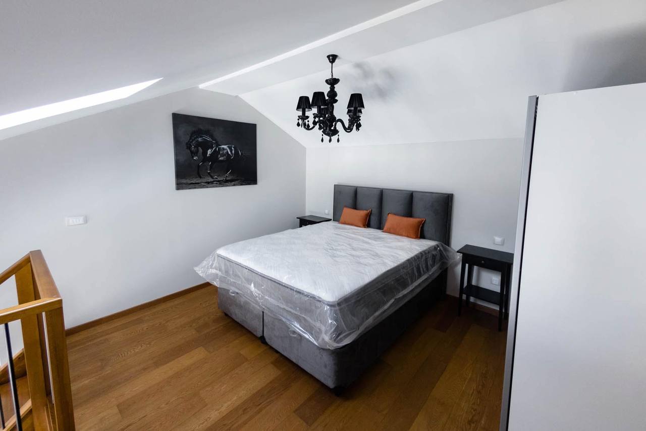 Modern attic bedroom in an apartment in Tivat, Montenegro: double bed, parquet flooring, and a black chandelier.