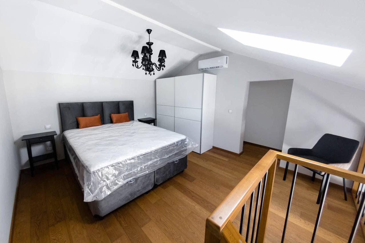Modern attic bedroom in an apartment in Tivat, Montenegro: a double bed, white wardrobe, and a stylish chandelier.