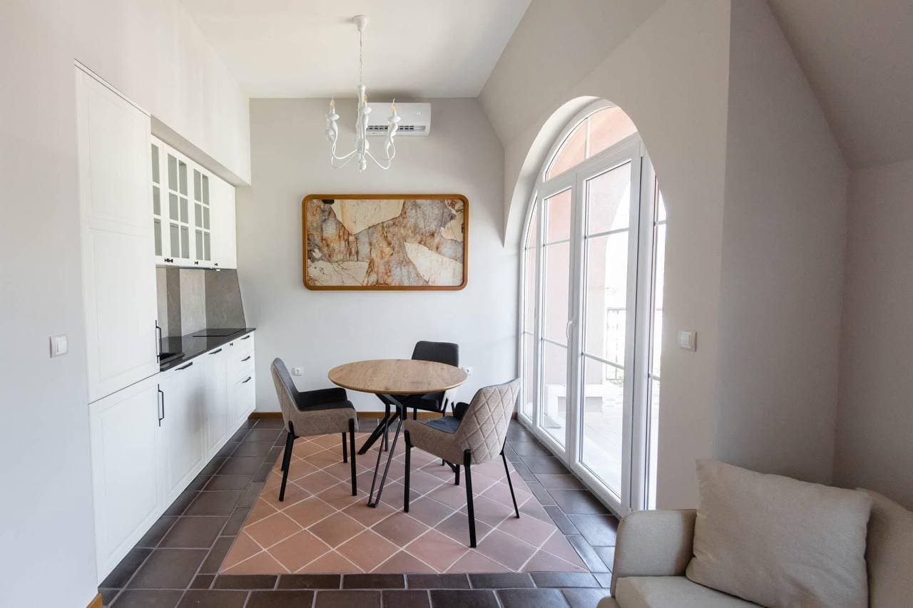 Modern kitchen-dining room in an apartment in Tivat, Montenegro: white furniture, dining area, and a panoramic arched window.
