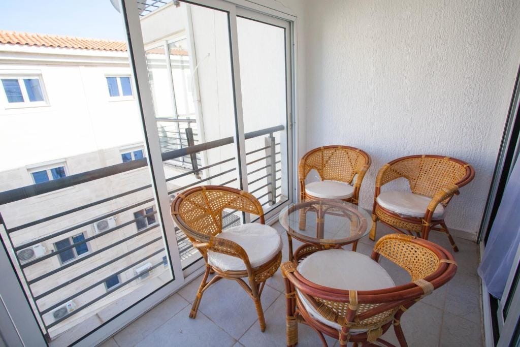 Cozy balcony with wicker furniture in an apartment in Budva, Montenegro: a glass table and four chairs with cushions.