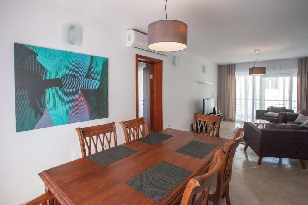 Living room interior with dining area in an apartment in Budva, Montenegro: wooden table, upholstered furniture, and panoramic windows.