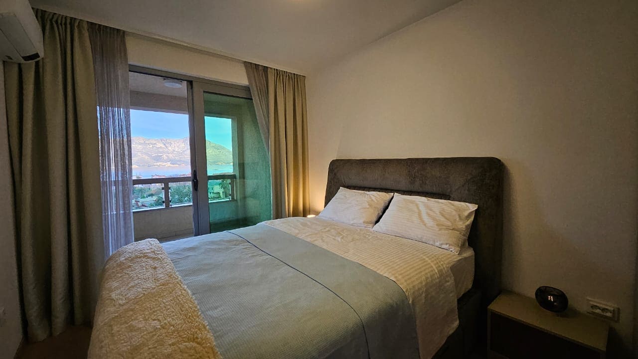 Bedroom in an apartment in Budva, Montenegro: double bed, panoramic window with mountain and sea views, balcony.