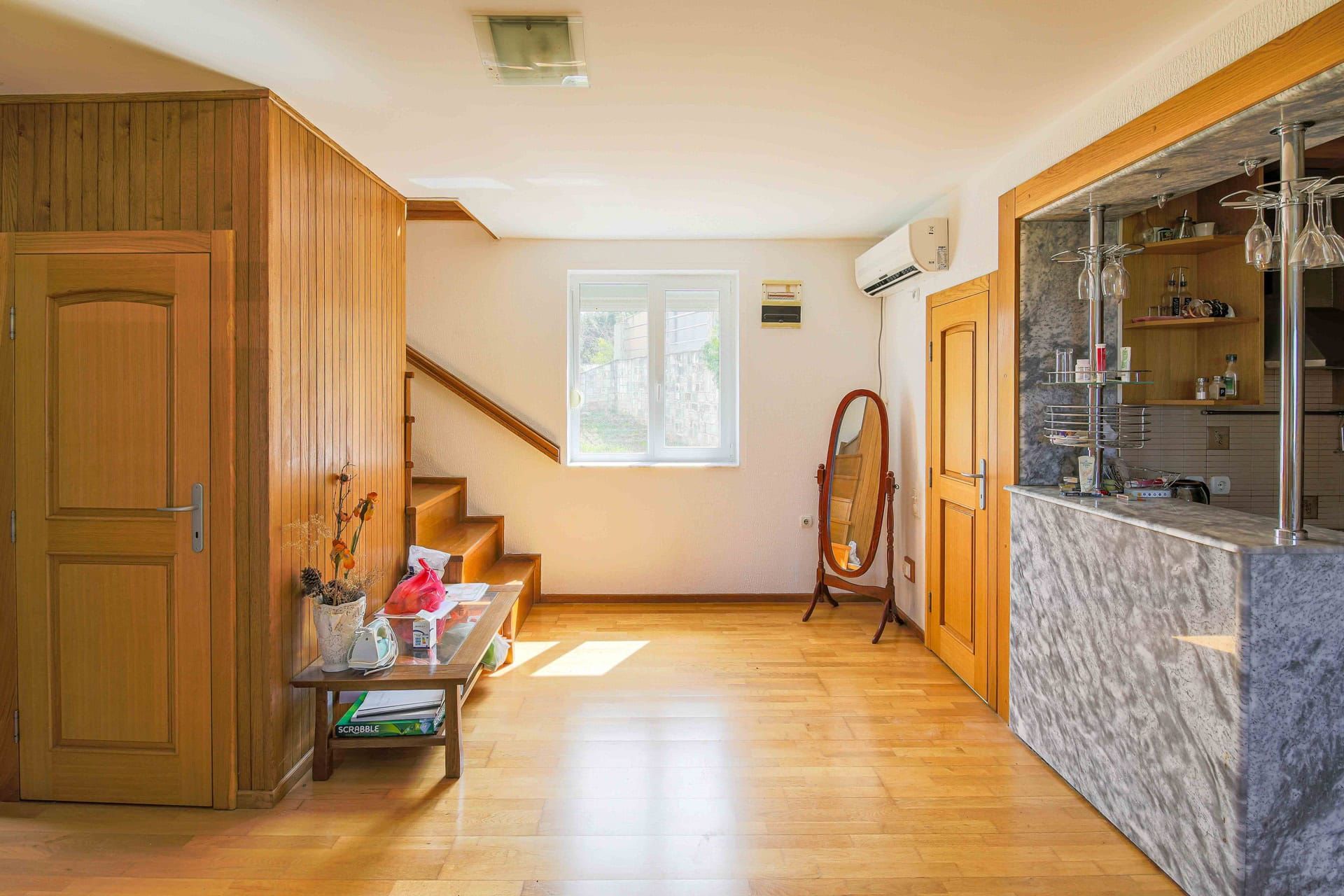 Living room with a wooden staircase and bar counter in a house for sale, Utjeha, Montenegro. Interior with parquet flooring.