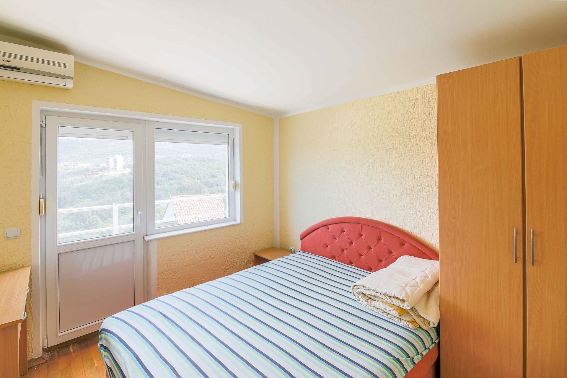 Bedroom in a house in Utjeha, Montenegro: double bed, wooden wardrobe, air conditioner, and mountain view from the window.