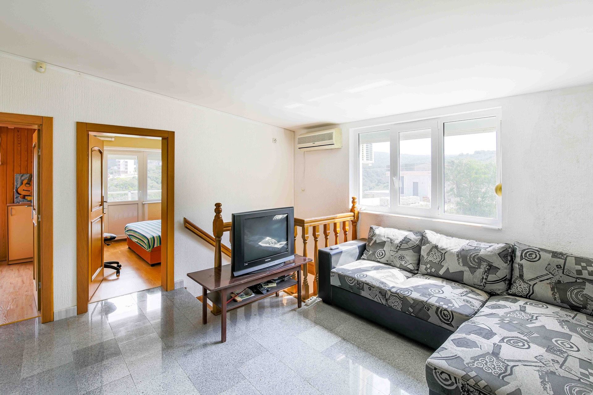 Living room with sofa and TV in a house for sale in Uteha, Montenegro: bright interior, stone floor, and mountain view.